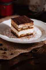 Tiramisu cake dessert served with coffee, biscuit and cocoa as ingredients on a bright white background. One piece