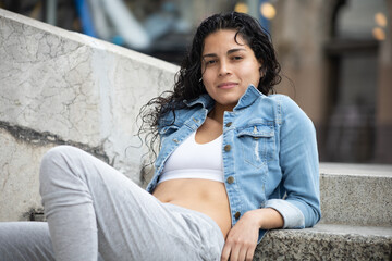 Girl sitting on the steps of the Palacio de Bellas Artes in Mexico City dressed in sportswear and a denim jacket