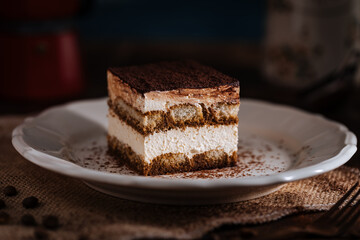 Tiramisu cake dessert served with coffee, biscuit and cocoa as ingredients on a bright white background. One piece