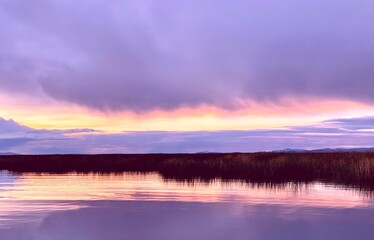 Violet sunrise over Titicaca lake at foggy morning.  Beautiful clouds reflection in calm water. Idyllic scene. Tranquility. Zen. Harmony.