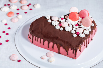 Pink heart shaped cake with chocolate glaze, meringues and macaroons on top as decoration. Placed on white plate. Valentine's day, mothers day, birthday, celebration concept.