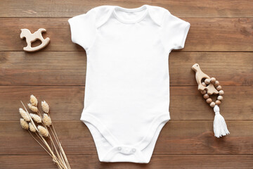 Mockup of white baby bodysuit on dark wood background with dried flowers and toys. Blank baby...