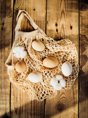 Easter concept. Beige mesh shopping bag with brown chicken eggs on a wooden background.