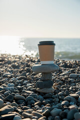 Coffee in a paper cup against the background of the sea. Sea pebbles. Sea surf.