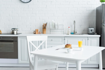 tasty pancakes, coffee and orange juice on white table in modern kitchen.