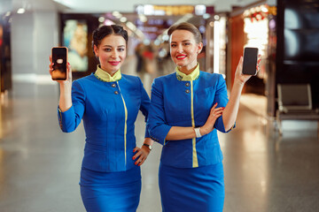 Joyful female flight attendants in aviation air hostess uniform looking at camera and smiling while...