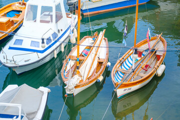 Fototapeta na wymiar Moored big and small boats reflected in clear water of Mediterranean sea at local fishing port in seaside town on sunny day in summer