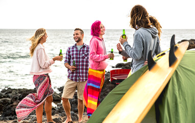 Young friends having fun together at beach camping party - Travel life style concept with happy people travelers drinking bottled beer at summer surf camp in Medano Tenerife - Bright warm filter