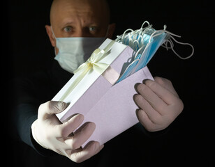 A man in a mask and gloves held out a congratulatory box with medical masks in his hands on a black...