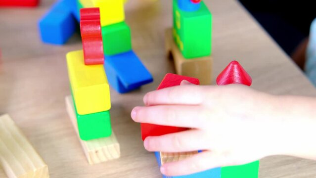 close-up of children's educational toys in hands of toddler, small child, a 2-year-old girl builds houses for characters from color blocks, concept of childhood, earlier child development, creativity
