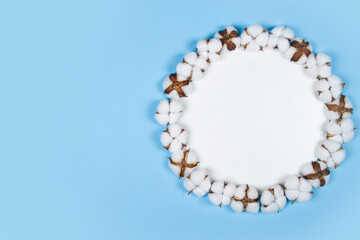 Round white frame of cotton flowers on light blue background with copy space