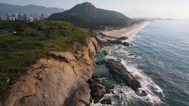 Aerial view of Praia do Secreto, a paradise in the west of Rio de Janeiro, Brazil. Big hills around. Sunny day at dawn. Beaches and mountains of Recreio dos Bandeirantes in the background. Drone takes