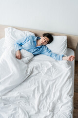 high angle view of young man in blue pajamas sleeping on white bedding.