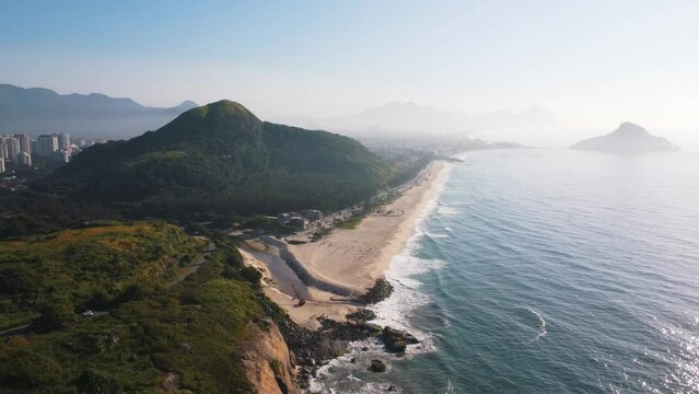 Aerial view of Praia do Secreto, a paradise in the west of Rio de Janeiro, Brazil. Big hills around. Sunny day at dawn. Beaches and mountains of Recreio dos Bandeirantes in the background. Drone takes