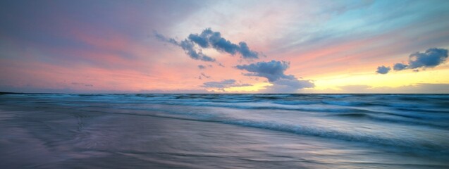Baltic sea at sunset. Dramatic sky, glowing clouds, soft golden sunlight. Waves, splashing water. Picturesque dreamlike seascape, cloudscape. Panoramic view, long exposure. Nature, weather themes