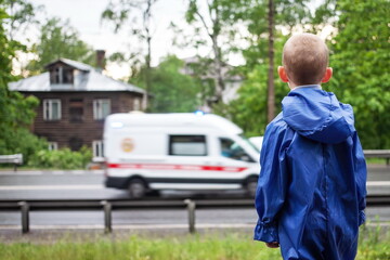 Little boy watching for ambulance car is passing on the road. Blurred motion, defocused.