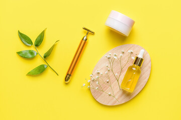 Face massage roller with cosmetic products on color background