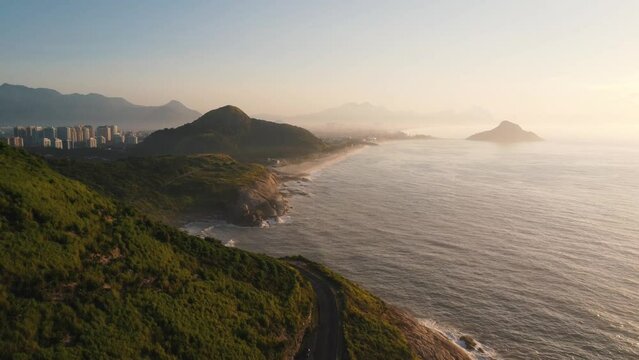 Aerial view of Prainha Beach, a paradise in the west of Rio de Janeiro, Brazil. Big hills around. Sunny day at dawn. Beaches and mountains of Recreio dos Bandeirantes in the background. Drone takes.