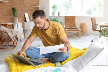 Handsome man working with document and laptop on bed at home