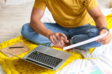 Young man working with document and laptop on bed at home, closeup