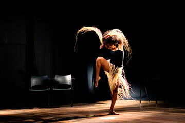 Contemporary dancer dancing in theater with black background and straw accessory.