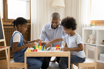 African family play wooden cubes, loving dad spend time with little son and daughter sit together at table in nursery enjoy playtime with colored bricks. Leisure game at home, kids development concept