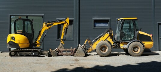 Yellow bulldozer and excavator face each other next to the hall. © Iwona
