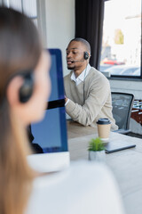 Fototapeta premium african american operator in headset talking near blurred colleague in office.