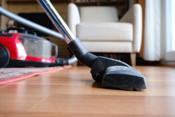 Someone using vacuum cleaner to clean wood home floor, closeup of cleaning room floor to remove...