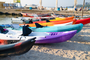 Colorful plactic kayaks or canoe on the beach sand for tourist rent. Surfing boards on stand during...