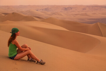 Fototapeta na wymiar Young woman sitting on sand in a desert near Huacachina, Ica region, Peru.