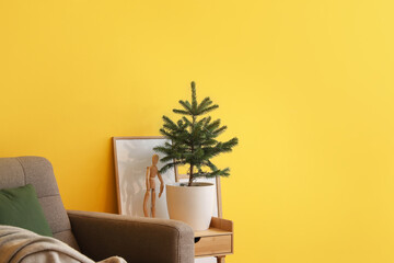 Small Christmas tree in flowerpot on table near color wall in room