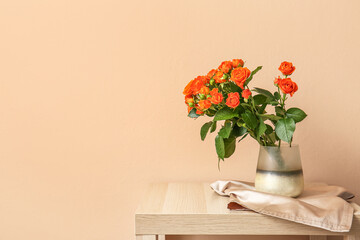 Vase with beautiful orange roses on table against beige wall