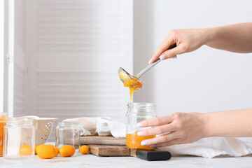 Woman pouring tasty kumquat jam into jar at kitchen table