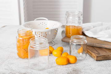 Jars with tasty kumquat jam on kitchen table background