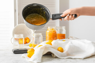 Woman pouring tasty kumquat jam into jar at kitchen table