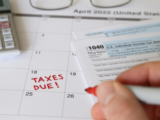 TAXES DUE! is shown written on a calendar by hand. The Internal Revenue Service IRS deadline in the USA for calendar year 2021 filing is April 18, 2022.