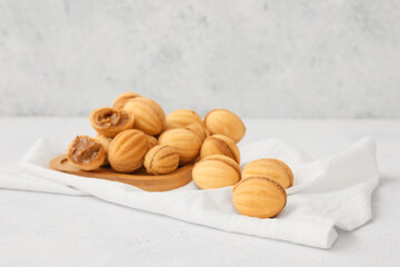 Wooden board of tasty walnut shaped cookies with boiled condensed milk on light background
