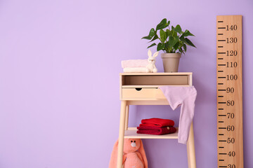 Houseplant, sweaters on standing desk and big wooden ruler near color wall