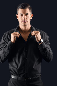Portrait of fashionable gentleman adjusting shirt on dark background