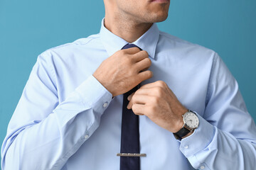 Young handsome man in formal clothes adjusting tie on color background, closeup - Powered by Adobe