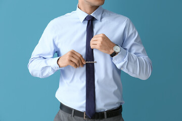 Handsome man in formal clothes adjusting tie on color background, closeup