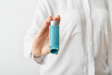 Woman holding asthma inhaler on light background, closeup