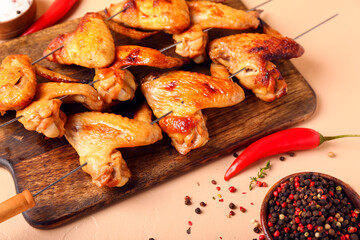 Wooden board with grilled chicken wings skewers on beige background