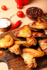 Wooden board with grilled chicken wings skewers on beige background