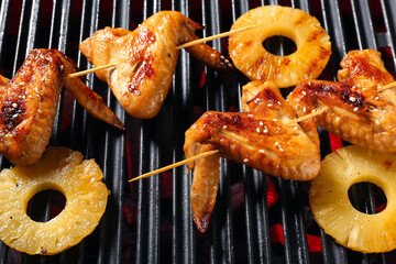 Tasty chicken wings skewers with pineapple slices on grill