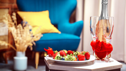 Blurred Strawberries on the plate with two champagne glasses and red heart on a table.