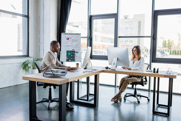 interracial business people in glasses looking at computer monitors while working in modern office.