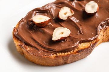 Bread with chocolate paste and hazelnuts on plate, closeup