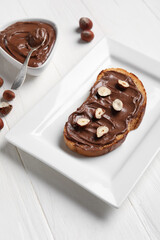 Plate of bread with chocolate paste and hazelnuts on white wooden background